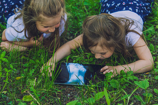 Children with the tablet lying in the grass in the meadow