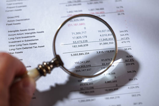 Magnifying glass on financial report Businessman holding a magnifying glass on a financial report concept for finance, balance sheet, tax or accounting financial statement stock pictures, royalty-free photos & images