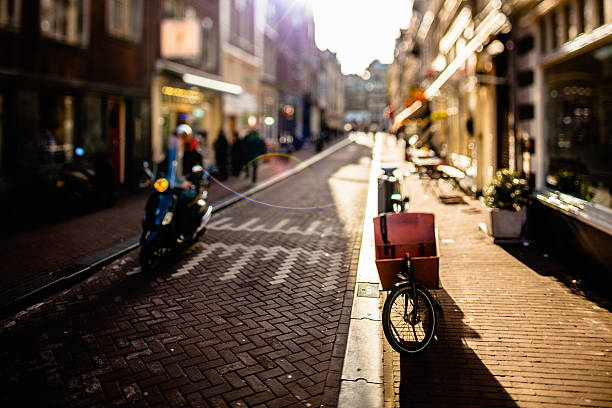 A scooter drives in an alley in the city of Amsterdam at sunset.
