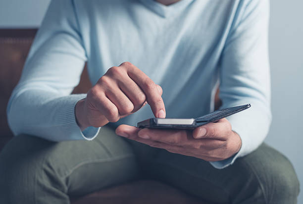 istock Young man sitting on sofa and using smart phone 478272288