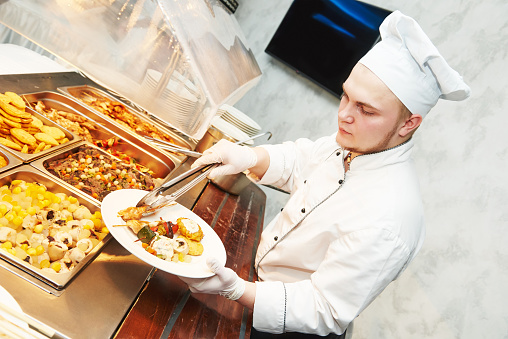 Catering services. young cook chef serving food at buffet