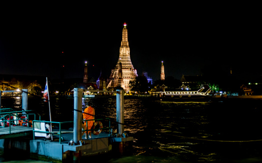 Bangkok, Thailand - November 1, 2013 - A Buddhist monk in a saffron-colored robe waits for the ferry on a pier on the Chao Phraya river opposite Wat Arun in Bangkok in November 2013.