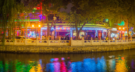 Beijing, China - September 30, 2013: Colourful neon signs illuminating the restaurants and bars lining the crowded shores of Houhai Lake, the popular night life district of Beijing, China's vibrant capital city. Panoramic image created from six contemporaneous sequential photographs.