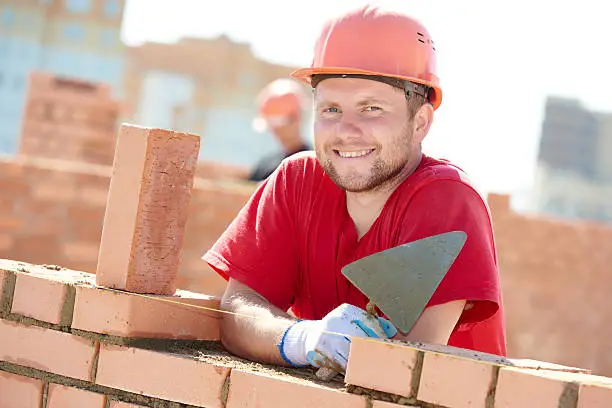 construction worker. Portrait of mason bricklayer installing red brick with trowel putty knife outdoors