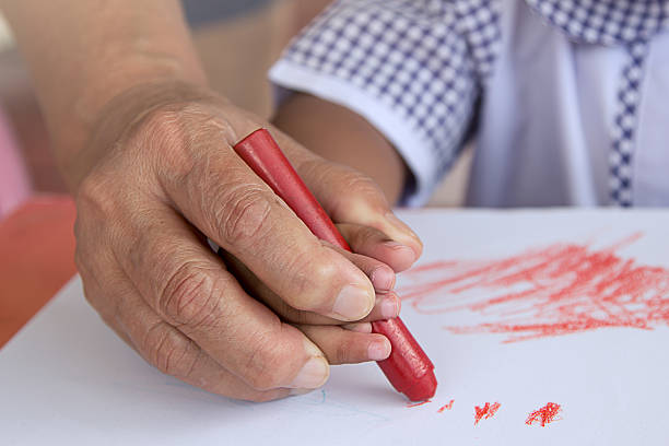 istock Grandma's hand holding child hand drawing with crayon 478295424