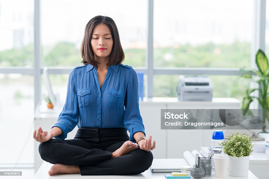 Meditation in office Asian businesswoman sitting on table and meditating Meditating Stock Photo