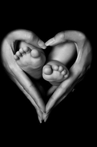 A black and white photograph of a mother holding her baby's feet in the shape of a heart.