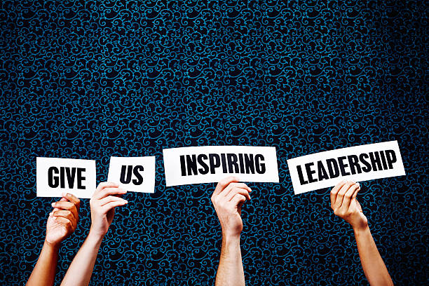 Four hands hold up words saying 'Give us inspiring leadership' against a darkly patterned background with copy space. Great leadership inspires everyone.