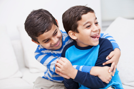 Brazilian twin boys (8 years) having fun, on living room sofa.