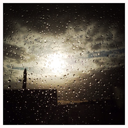 Raindrops on a window. With a overcast sky behind it. The sun is about to break through. The image was taken shortly before sunset after a day with both rain and sunshine.