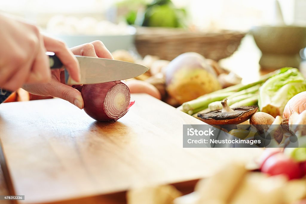 Cropped image of woman cutting onion at table Close-up cropped image of woman chopping onion. There are healthy vegetables on table. Focus is on knife and vegetable. Female is preparing food, She is in domestic kitchen. 2015 Stock Photo