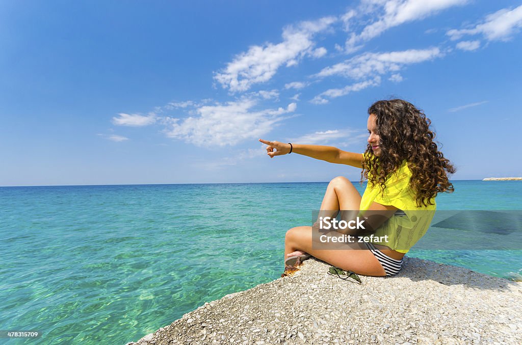 Plage teen femme avec des cheveux bouclés pointant du doigt l'horizon de l'océan - Photo de Activité libre de droits