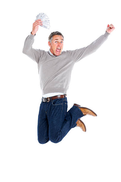 Portrait of excited mature man holding money jumping in air over white background