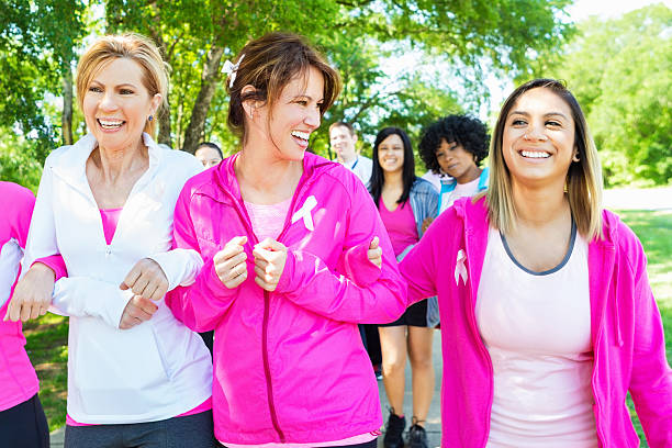 Diverse women walking in breast cancer awareness marathon race Team of mature and young adult women are walking together, arm in arm, as they cross the finish line at a breast cancer awareness marathon or 5k race. They are smiling together. Caucasian and Hispanic women are wearing pink athletic clothing and breast cancer awareness ribbons. walking for a cause stock pictures, royalty-free photos & images