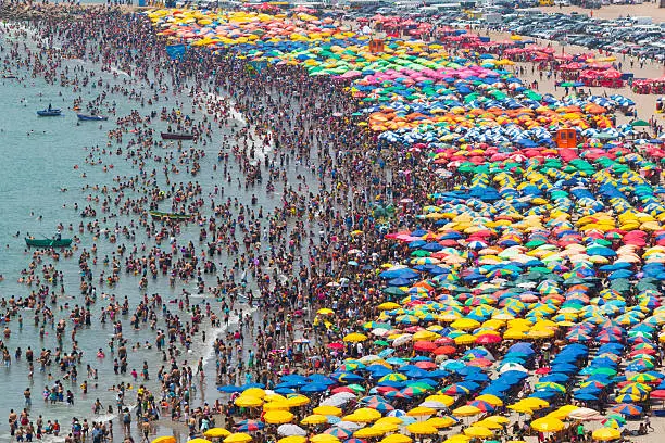 crowded beach with umbrellas and people in the water