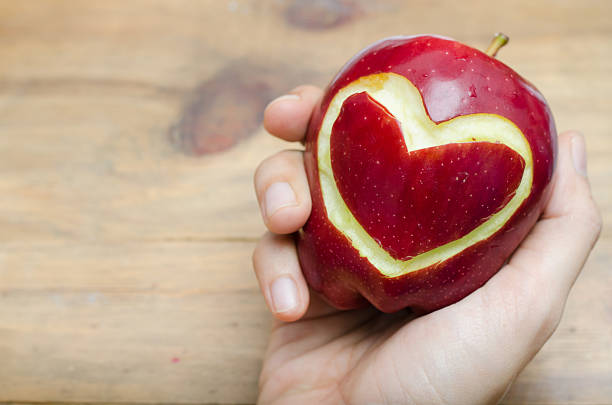 istock Apple,heart in woman hand on wood table 478336600