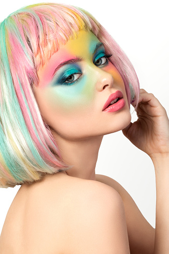 Portrait of young woman with funny rainbow coloured make-up touching her hair