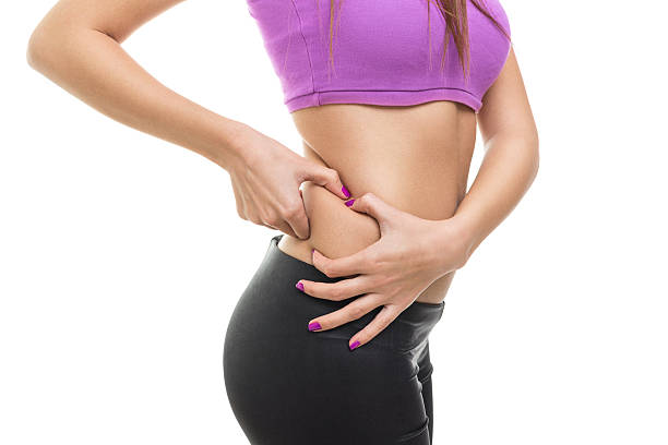 Closeup of slim young woman pinching pot belly Closeup studio shot of slim young woman pinching pot belly or love handles wearing short purple top and black leggings. Isolated on white background. Fitness, diet and body care concepts. pot belly stock pictures, royalty-free photos & images