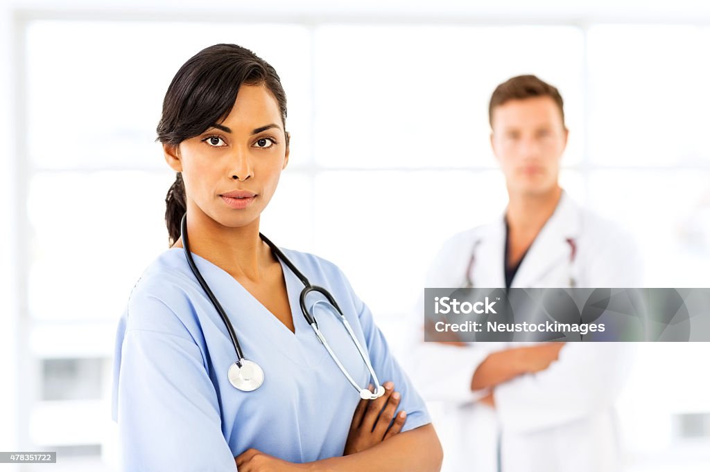 Confident Female Nurse In Hospital Portrait of confident female nurse with male doctor in background at hospital. Horizontal shot. 20-24 Years Stock Photo