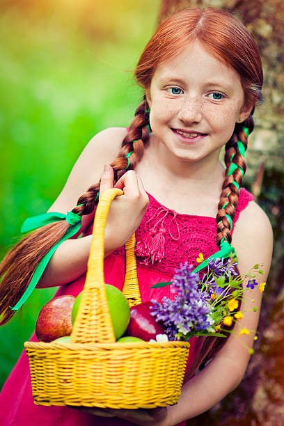 Happy child holding a basket with apples and flowers outdoors in summer