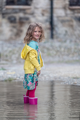 A child stands rubber boots in a deep puddle an look into the cam.