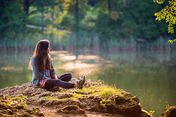 young women enjoy the evening sun at the rock at a lake.