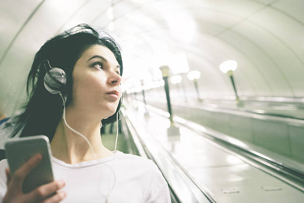 Beautiful Woman Listening Music On Her Smartphone While On Escalator Beautiful woman listening to music from her smartphone while on subway escalator. russian culture audio stock pictures, royalty-free photos & images