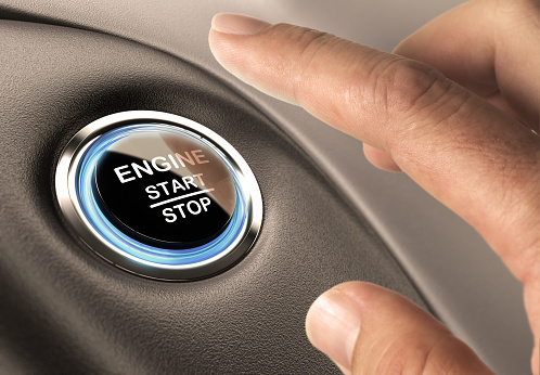 Car engine start and stop button with blue light and black textured background, close up and one finger