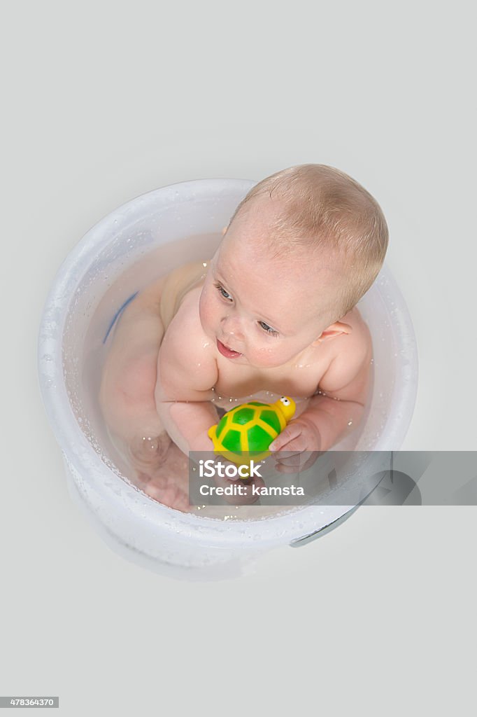 Cute baby in transparent bucket and playing with toys Little girl having a bath in the transparent bathing bucket and playing with rubber turtle. 2015 Stock Photo