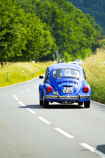 Essen, Germany - June 14, 2015: People are driving with blue VW Beetle oldtimer on rod Schuir into valley Ruhr in south of Essen in summer. At back of car is old country code Denmark.