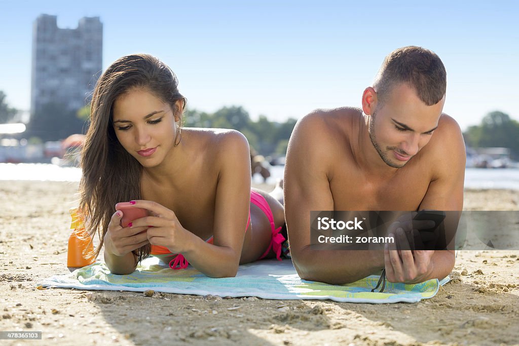 Texting Beautiful young couple on beach, texting Phone Message Stock Photo