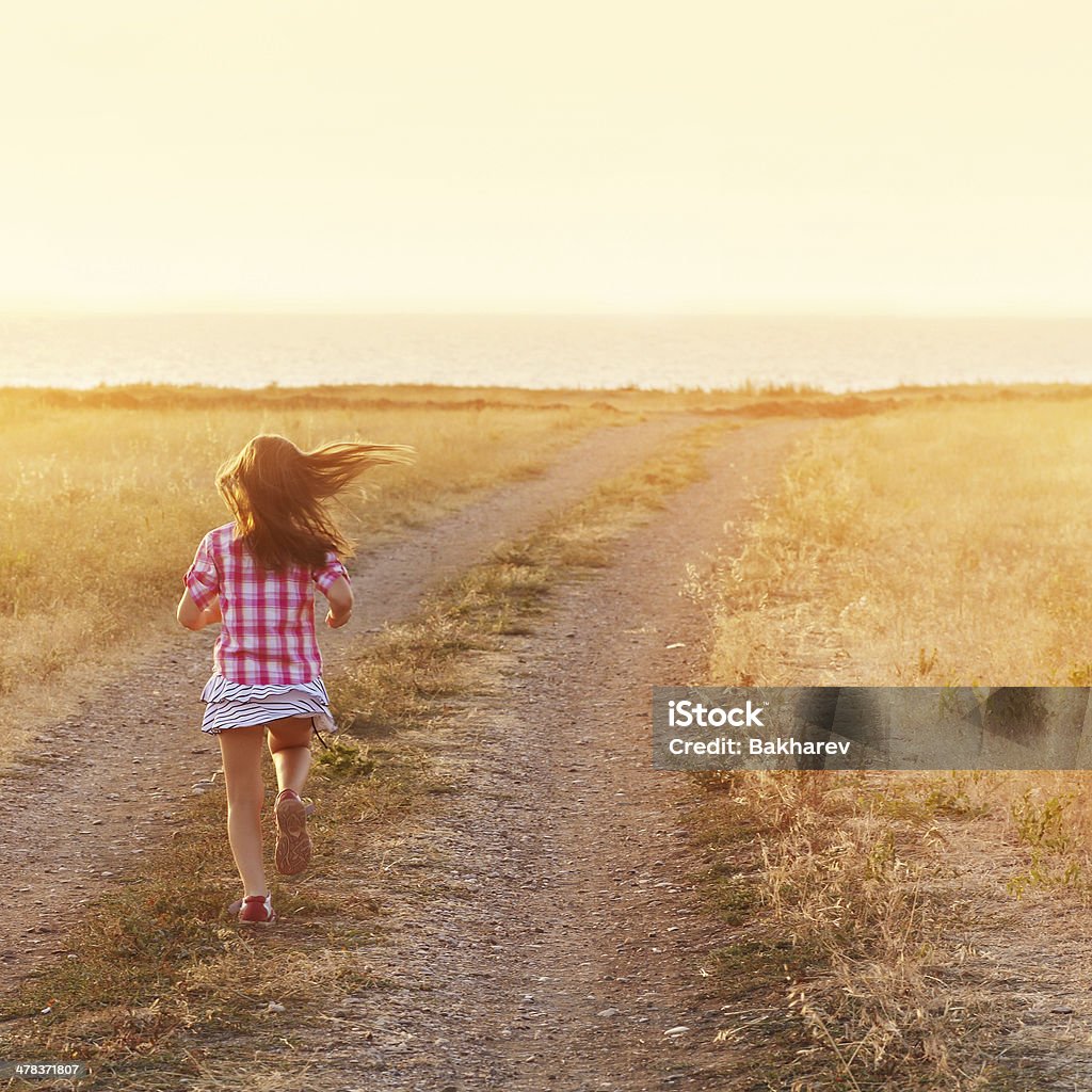 Little girl running in backlit meadow Little girl running down the road at sunset Back Lit Stock Photo