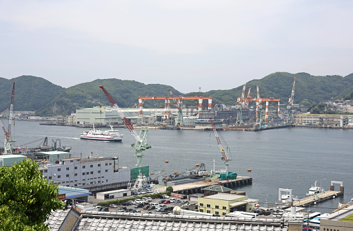 Nagasaki, Japan - May 27, 2015: Industries on the Waterfront of Nagasaki Bay, Japan. Commercial docks and marine cargo terminals with red and white cranes along the natural harbor.