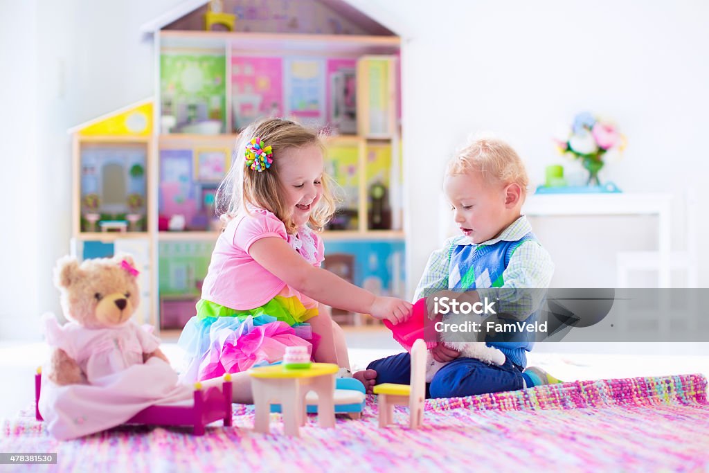 Kids playing with stuffed animals and doll house Kids playing with doll house and stuffed animal toys. Children sit on a pink rug in a play room at home or kindergarten. Toddler kid and baby with plush toy and dolls. Birthday party for little child. 2015 Stock Photo