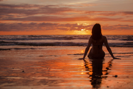 Woman seated on a beach looking at sunset