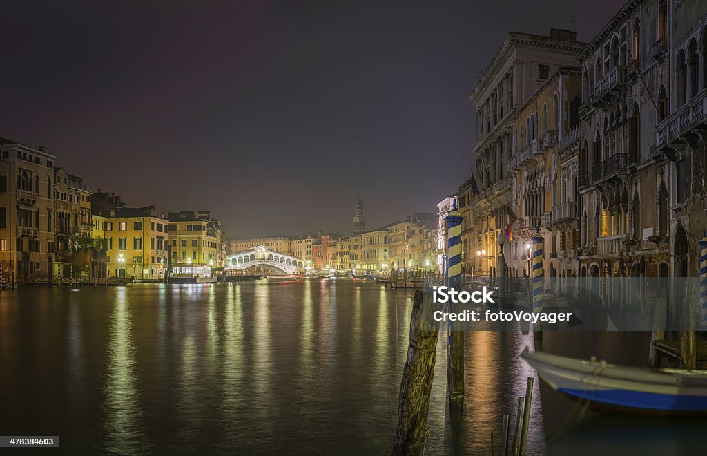 Venice Grand Canal Palazzo and Rialto Bridge at night Italy The iconic stone arch of Rialto Bridge illuminated in the blue dusk above the broad sweep of the Grand Canal between the busy restaurants, historic palazzo, gondolas and boats of the San Marco and San Polo quarters of Venice, Italy.  ProPhoto RGB profile for maximum color fidelity and gamut. Arch - Architectural Feature Stock Photo