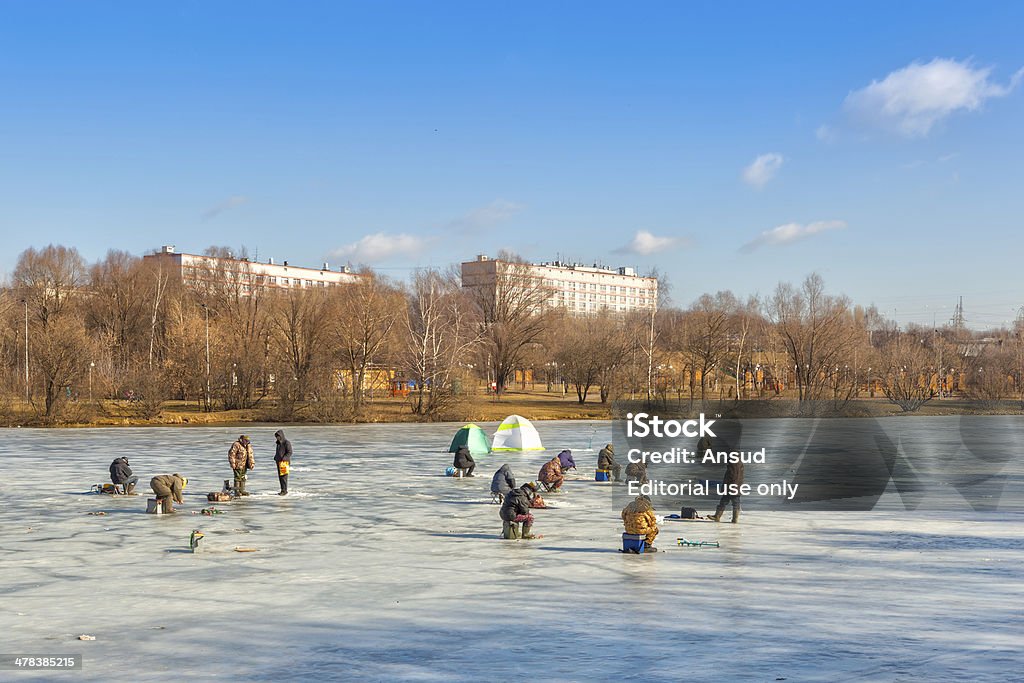 Fishermen sitting and walking on ice of Lyublino pond Moscow, Russia - March 9, 2014: Fishermen sitting and walking on ice of Lyublino pond in bright sunny day with urban buildings at back. Activity Stock Photo