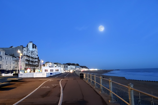 Hastings promenade in the early evening looking towards the East Hill area. There is a bright full moon showing in the sky.