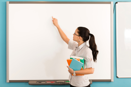 Portrait of young teacher standing in front of the whiteboard in the classroom.