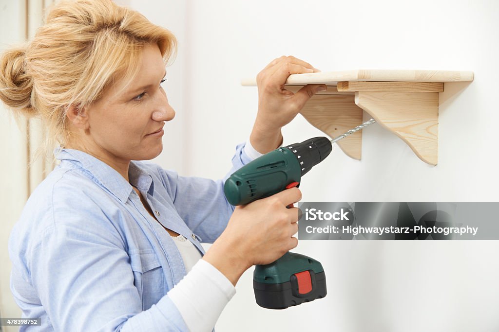 Woman Putting Up Wooden Shelf At Home Using Cordless Drill Shelf Stock Photo