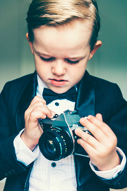 istock Boy wears tuxedo and plays with old retro camera 478403958