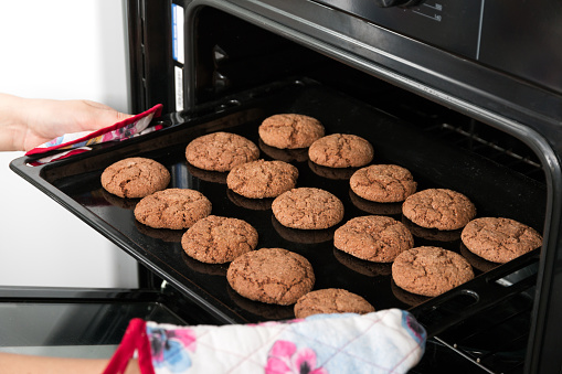 Woman getting roasting pan with oat cookies out of oven