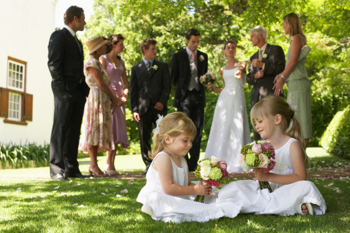 Cute little bridesmaids holding bouquets with guests in background