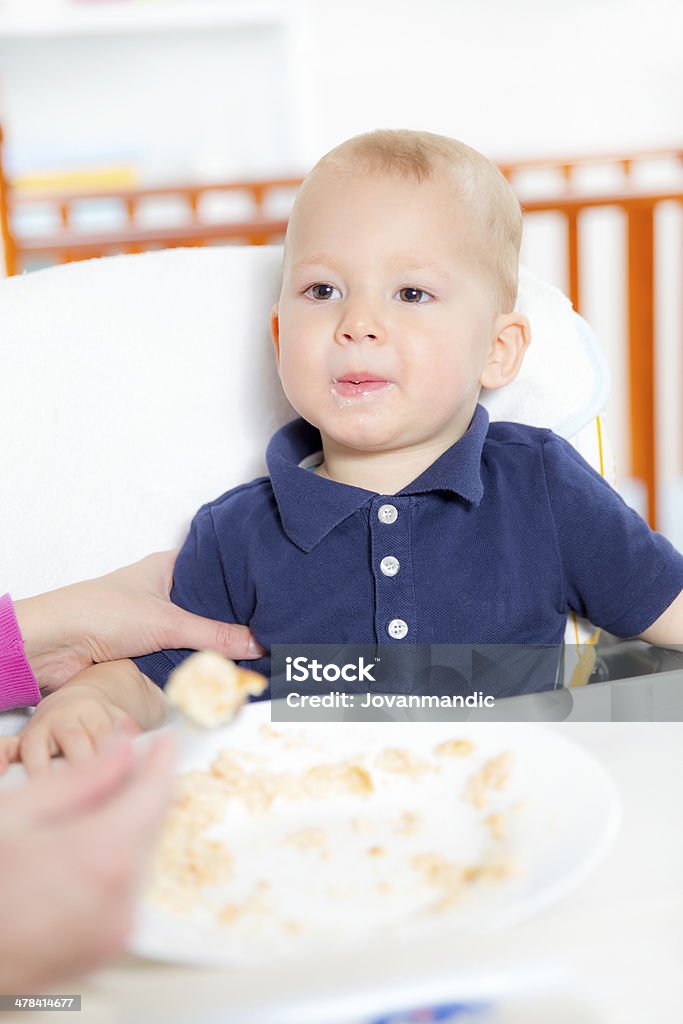 Cute baby boy eating, sitting in a highchair. 12-17 Months Stock Photo