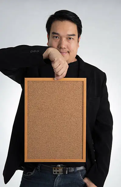 Asian man in black suit holds an empty woodboard , on a gray background