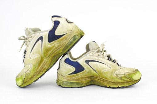 An old pair of grass stained sneakers on a white background.