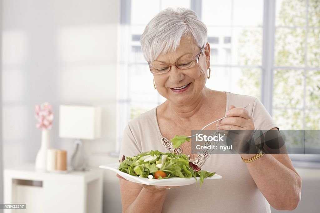 Old lady eating green salad Happy old lady eating fresh green salad, smiling.. Senior Adult Stock Photo
