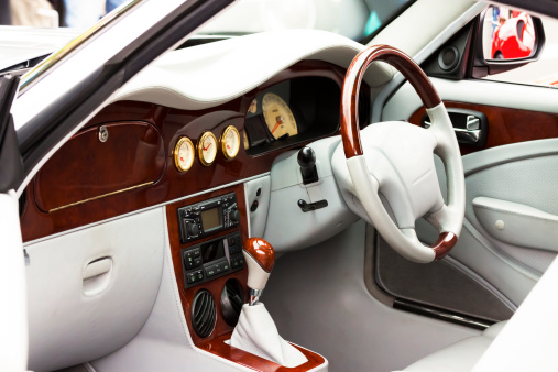 Closeup interior of white luxury sports car with white leather and dark wood steering wheel and dashboard, full frame horizontal composition