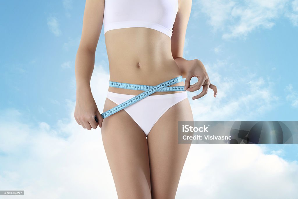 woman holding blue meter with hands near waistline woman holding blue meter with hands near waistline, on a sky background. Abdomen Stock Photo