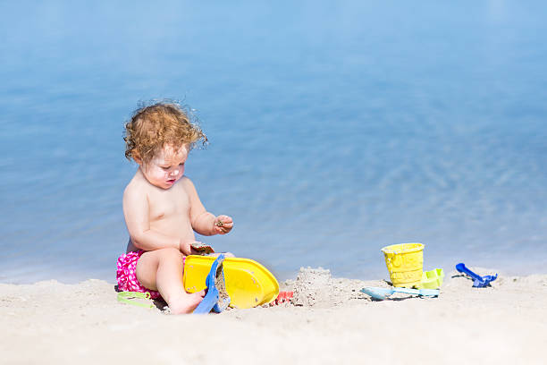 Funny baby girl playing on beautiful beach with blue water Funny baby girl playing on a beautiful beach with clear blue water backside for a girl on the beach stock pictures, royalty-free photos & images